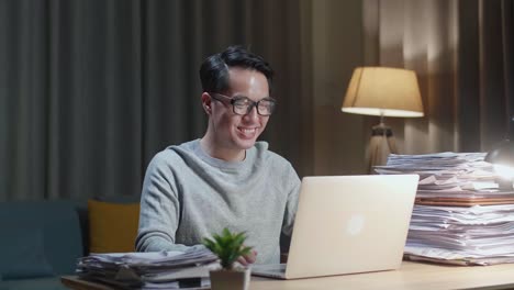 아시아인 남자가 집에서 문서로 작업하는 동안 노트북으로 비디오 통화를 하고 있습니다.