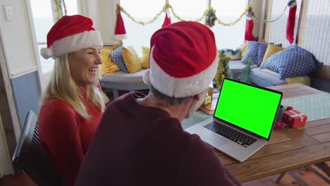 Smiling-caucasian-couple-in-santa-hats-making-laptop-christmas-video-call,-with-green-screen