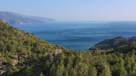 Breite-Luftaufnahme-Der-Überreste-Des-Verlassenen-Kajak-Dorfes-Mit-Einem-Letzten-Gebäude-Auf-Einem-Hügel-Mit-Blick-Auf-Das-Blaue-Mittelmeer-An-Einem-Sommertag-In-Fethiye,-Türkei