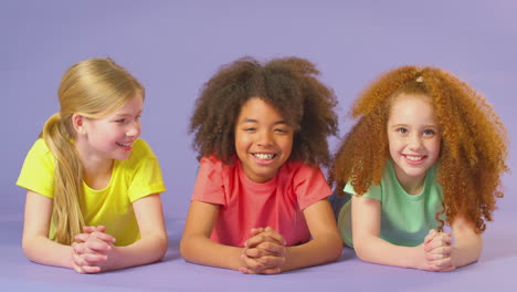 studio portrait shot of three children friends lying on floor against purple background