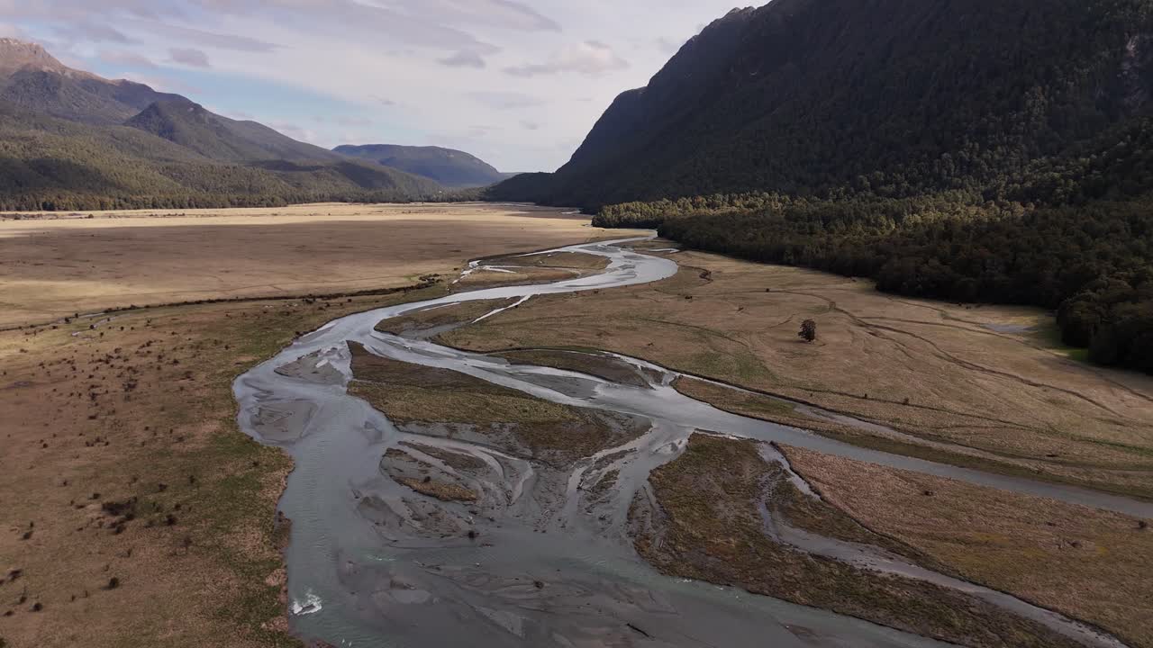 Una ripresa cinematografica all'indietro con un drone che rivela un ruscello di montagna incontaminato che scorre attraverso le cime innevate delle Alpi meridionali sulla strada per Milford Sound, Nuova Zelanda
