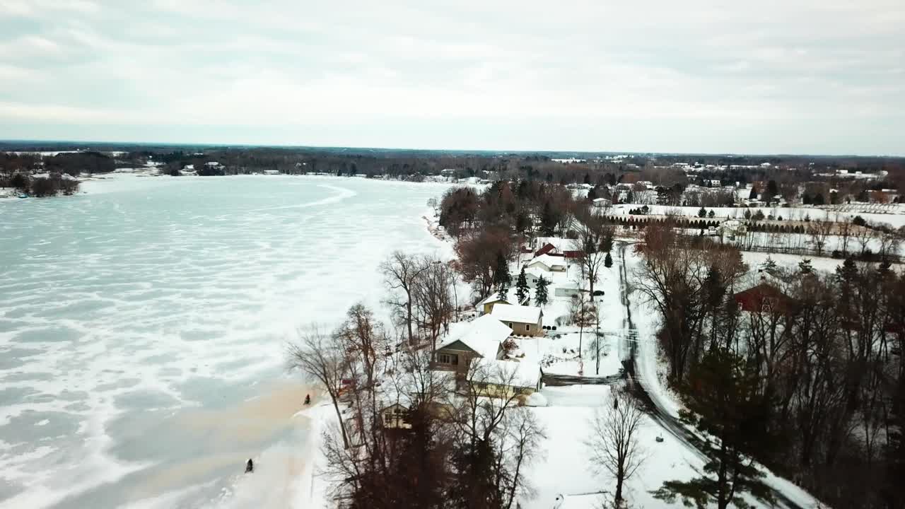 Aerial flyover snowmobilers riding on frozen lake during winter. 4K
