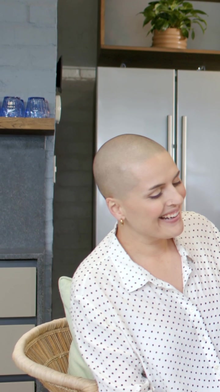 Video verticale: Donna che si gira e ride su una sedia di vimini in cucina dopo una battuta, indossando una camicetta a pois.