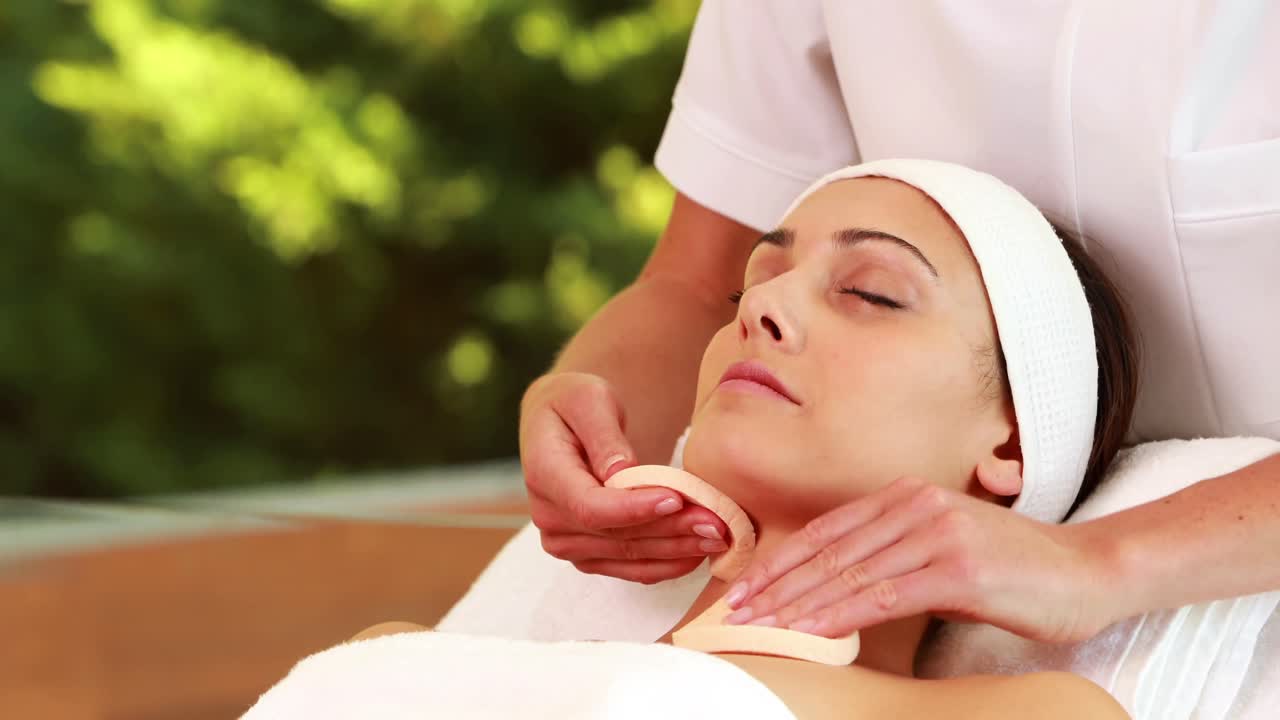 una morena sonriente recibiendo un bonito masaje facial