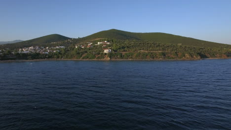 Drone-flying-from-sea-to-the-shore-with-houses-on-waterfront-Greece