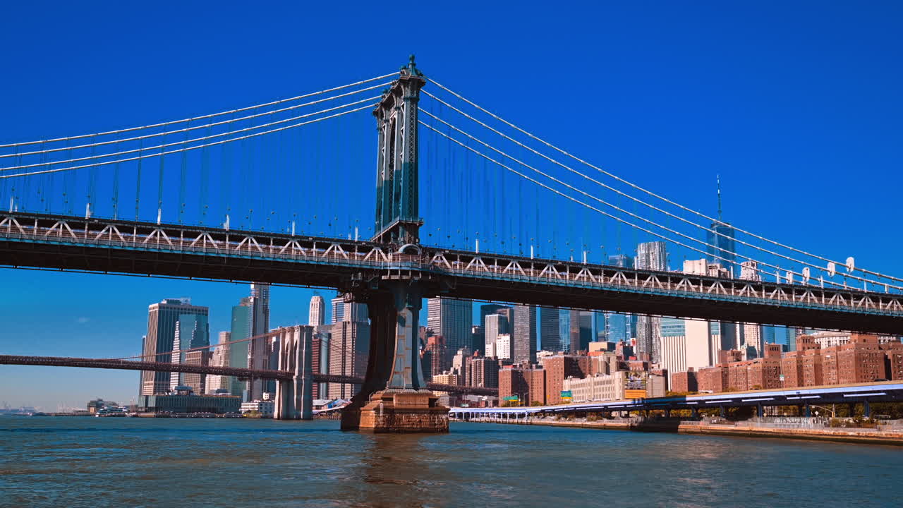 Vista del Manhattan Bridge dal traghetto dell'East River. Il traghetto naviga sotto il Manhattan Bridge con lo skyline di New York sullo sfondo.