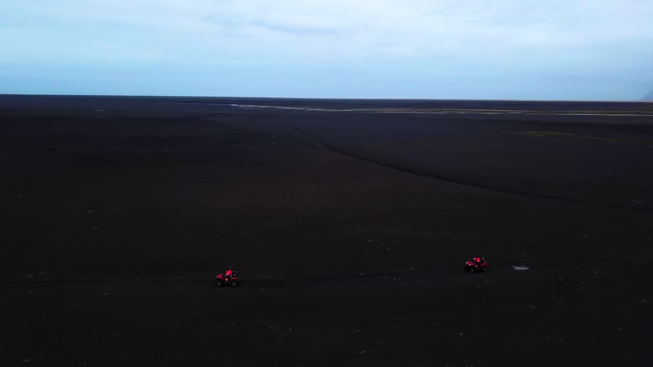 Aerial view of bright red quad bikes speeding off road on Iceland black sand beach