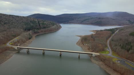 This-is-a-360-degree-drone-pan-of-a-pristine-mountain-lake-with-a-bridge-crossing-it-during-late-autumn