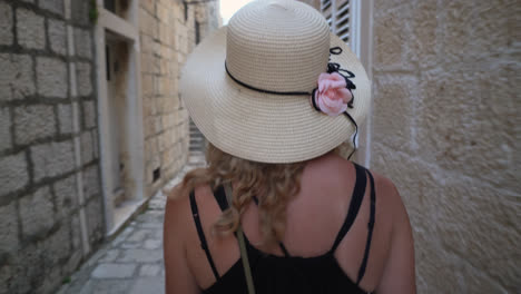 caucasian female tourist wearing a summer hat is walking on the alley of historic town in croatia. tracking shot