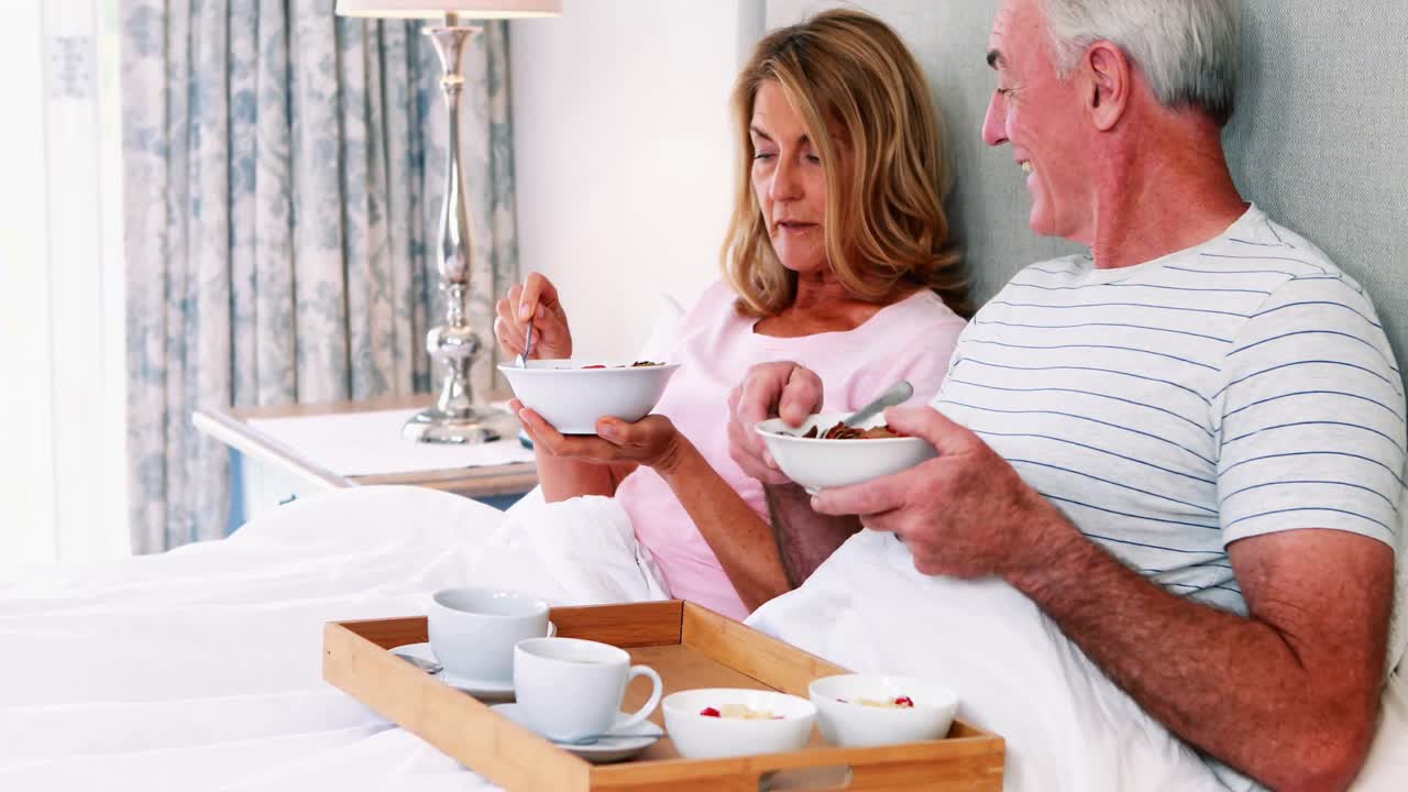 Smiling senior couple having breakfast on bed