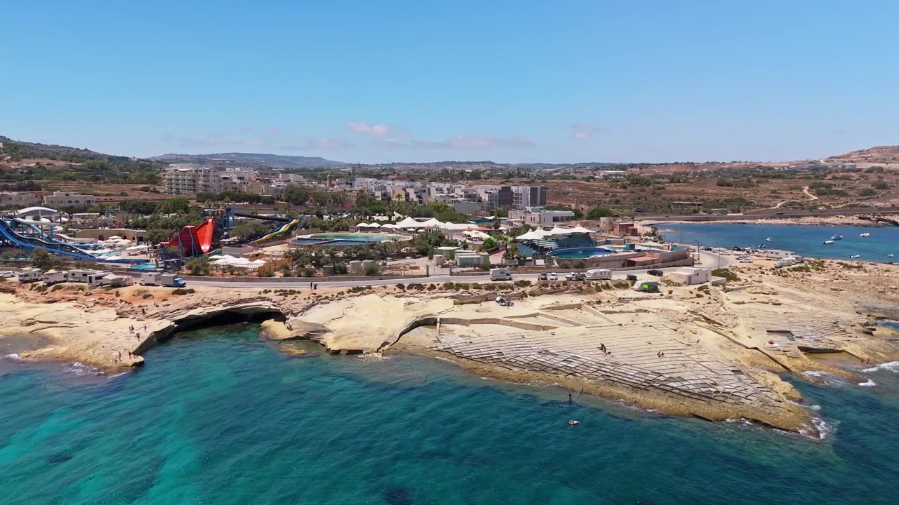 Baħar iċ-Ċagħaq, Malta, parco acquatico con scivoli e piscine lungo la costa mediterranea, famiglie e bambini che si godono attività ricreative in riva al mare in una giornata di sole, vista aerea