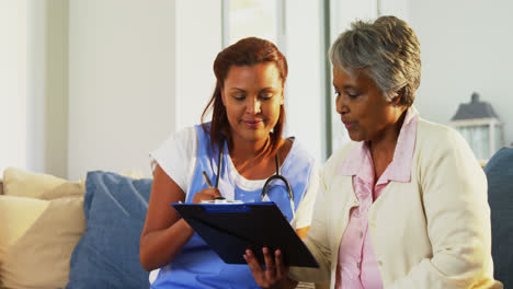 doctor explaining medication on clipboard to senior woman in living room 4k