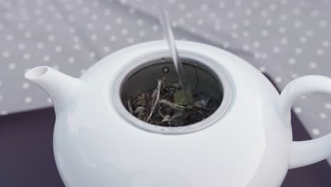 hot water pooring on fresh tea leaves in a porcelain teapot