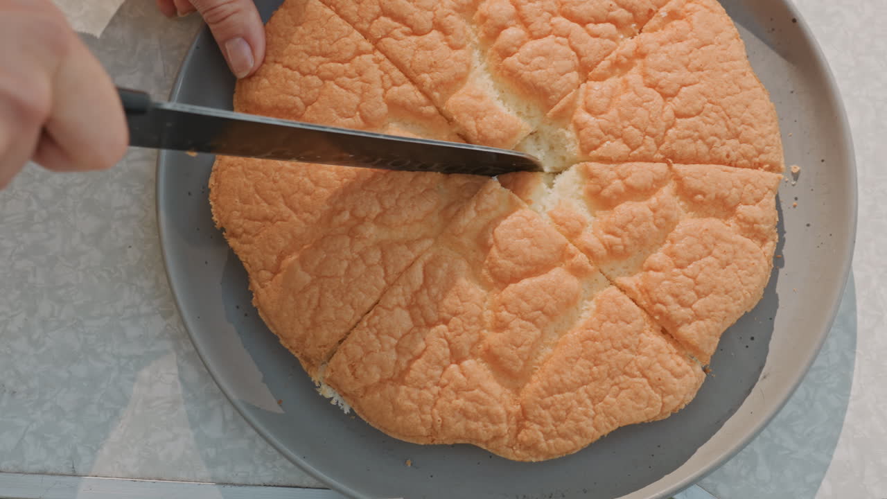 Tavolo da campeggio illuminato dal sole con fette a spicchio servite da mani, mollica morbida e crosta dorata visibili sul piatto, atmosfera amichevole da picnic con tavolo con piano laminato e fogliame verde in lontananza, dessert informale.