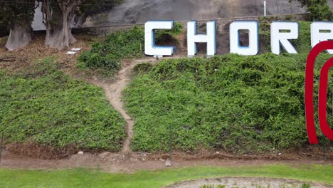 video de drone de un letrero rojo que dice "perú" y detrás de él en una colina verde otro letrero que dice "chorrillos" el nombre del distrito en el que se grabó esto