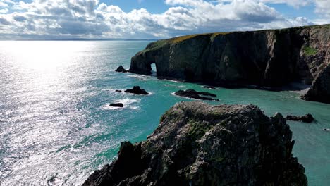 Drones-Volando-Sobre-Seastack-Con-Pájaros-Anidando-En-El-Promontorio-Con-Cuevas-Marinas,-Mares-Verde-Esmeralda-Y-Cielo-Dramático-En-La-Costa-De-Cobre-En-Waterford,-Irlanda