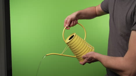 yellow watering can poured by adult man in front of chroma green screen