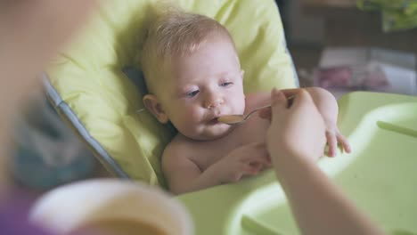 mommy feeds cute boy with fresh soup puree in highchair