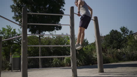 a man pulls himself up onto a pull up bar in slow motion during a workout in a park