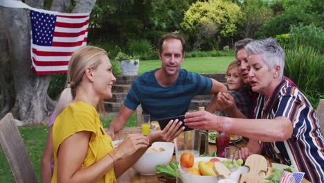 smiling caucasian family having celebration meal in garden looking at smartphone together