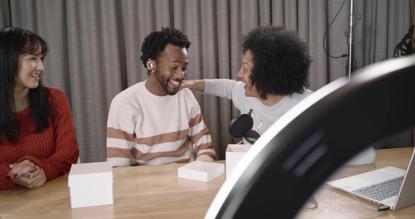 African American hosts opening boxes, showing white case, reviewing earbud fit near mic in studio