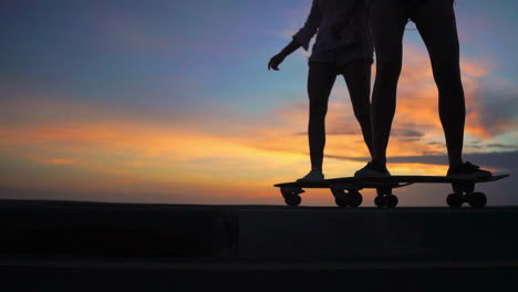 against the backdrop of mountains and a gorgeous sky, two friends ride skateboards on a road at sunset, captured in slow motion. they're in shorts