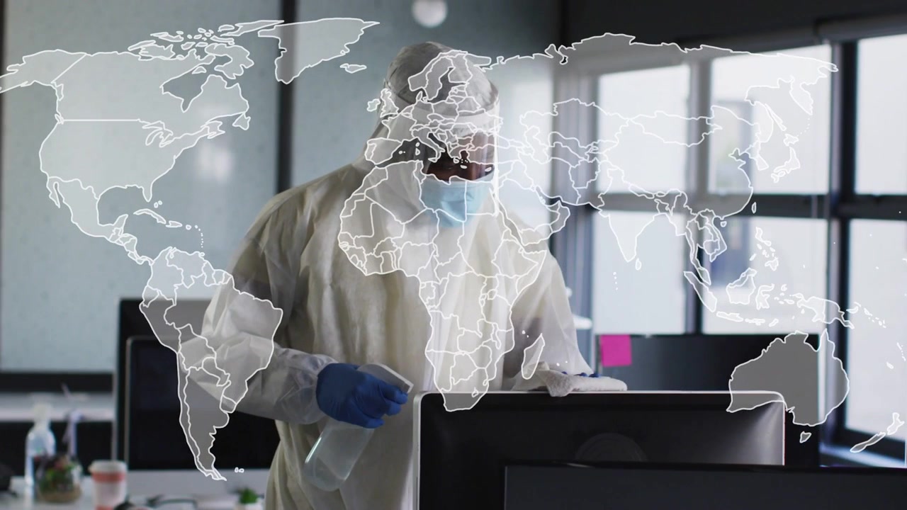 Addetto alle pulizie che si avvicina a una scrivania, spruzza e pulisce un monitor per sicurezza, con una sovrapposizione di mappa sulla scena.