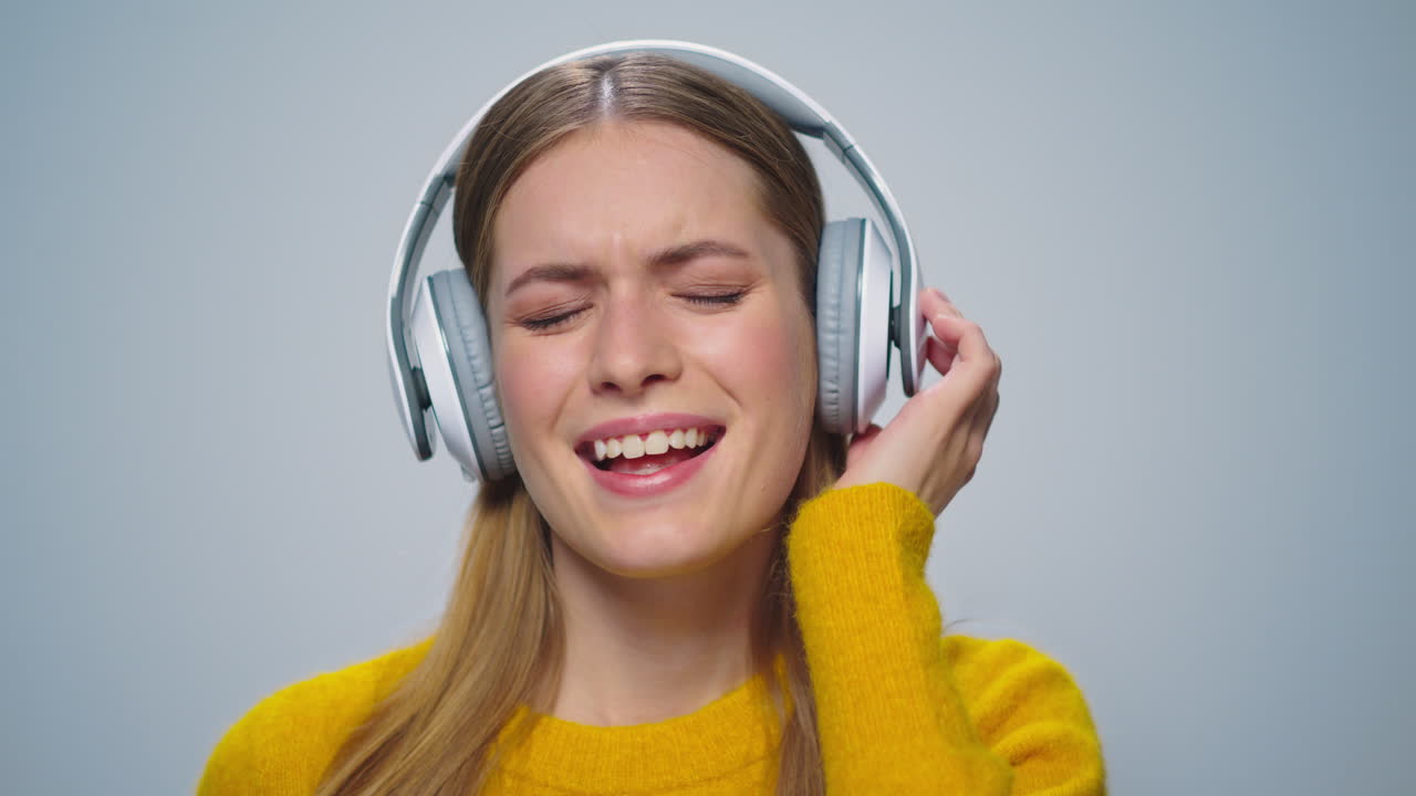 mujer sonriente de primer plano escuchando música en auriculares sobre un fondo gris.