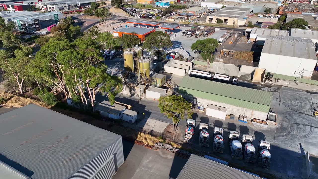 Drone view featuring an industrial area with loaders and trucks at parking lot during daytime.