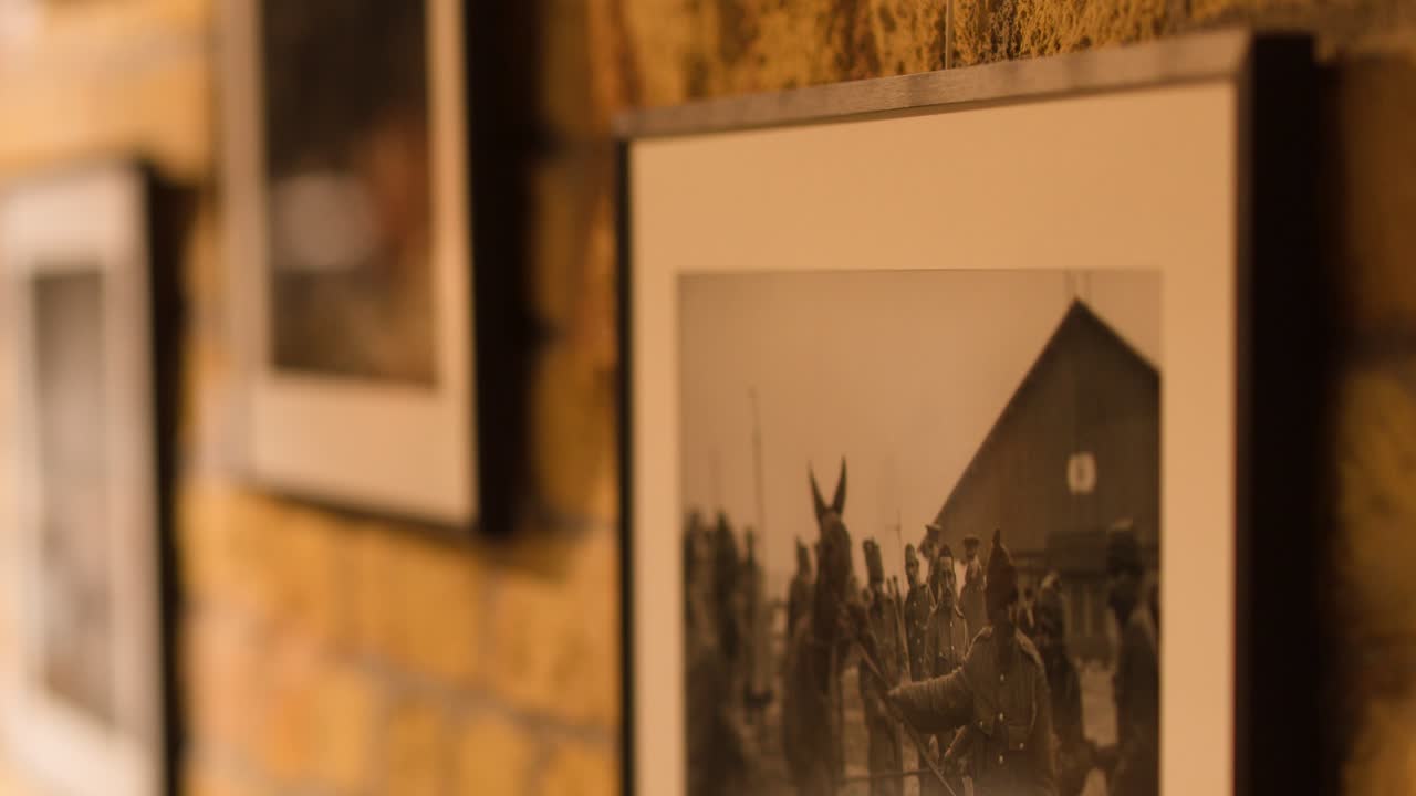 Pareti di un museo illuminate in modo caldo espongono fotografie in bianco e nero incorniciate risalenti al periodo bellico, con la telecamera che si sposta lentamente lateralmente
