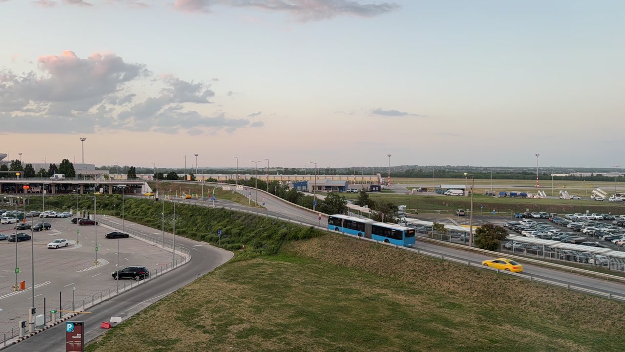 Pôr do sol sobre um aeroporto com carros e ônibus circulando na estrada. Rastros de luz dos veículos com o céu mudando do dia para a noite