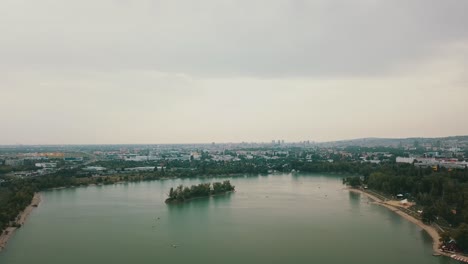 Drone-shot-of-the-lake-Zlate-Piesky,-Bratislava,-Slovakia-on-a-cloudy-day-with-the-city-in-the-background