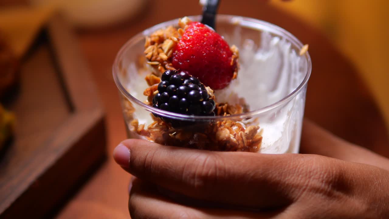 Gros plan sur une main dégustant un parfait au yaourt sain avec du granola et des baies