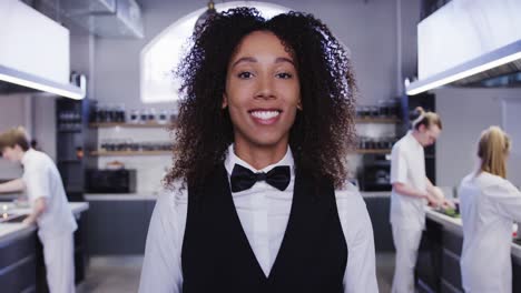 african american female restaurant manager in the kitchen, looking at camera, smiling