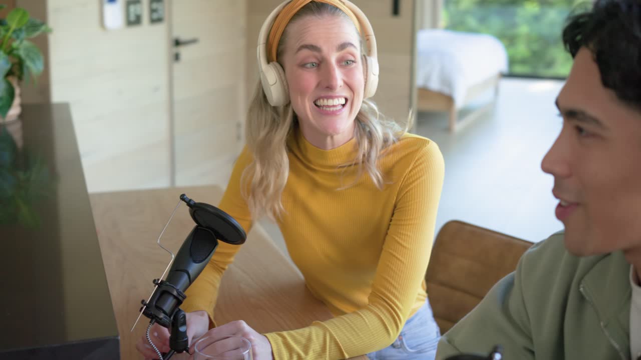Laptop, donna bianca e uomo asiatico che parlano nei microfoni e registrano un podcast in studio