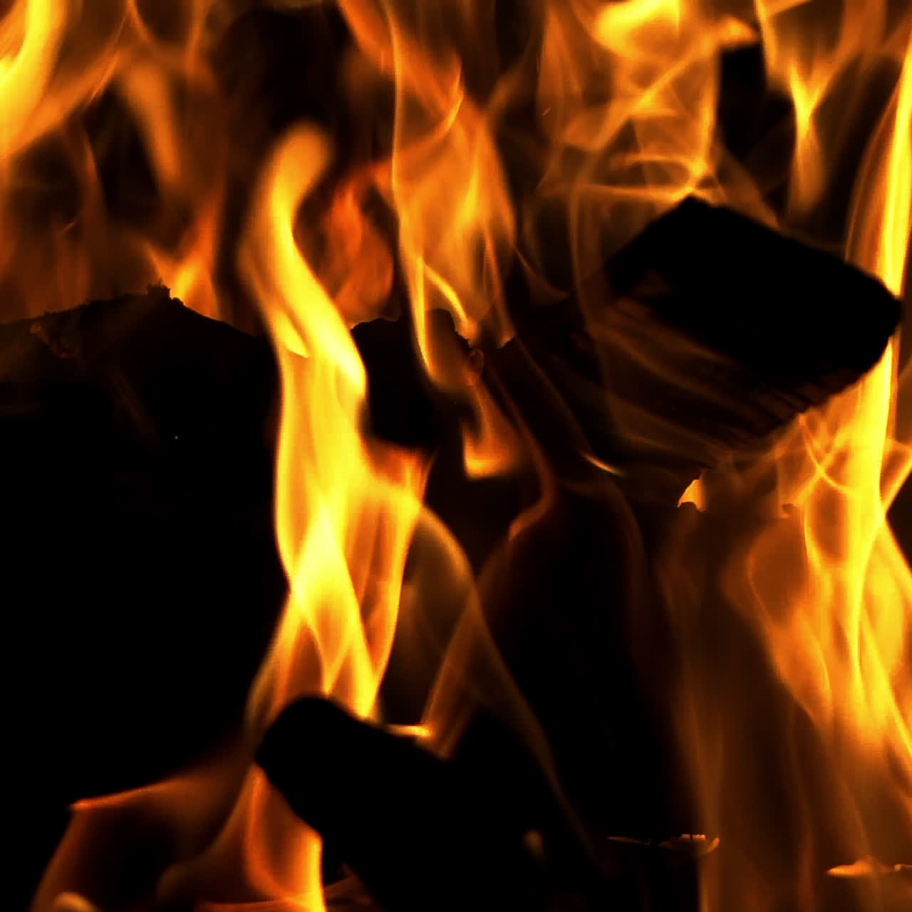 Ceppi neri all'interno della fiamma brillante che brucia di notte su sfondo scuro. Fiamma rossa che si alza. Primo piano