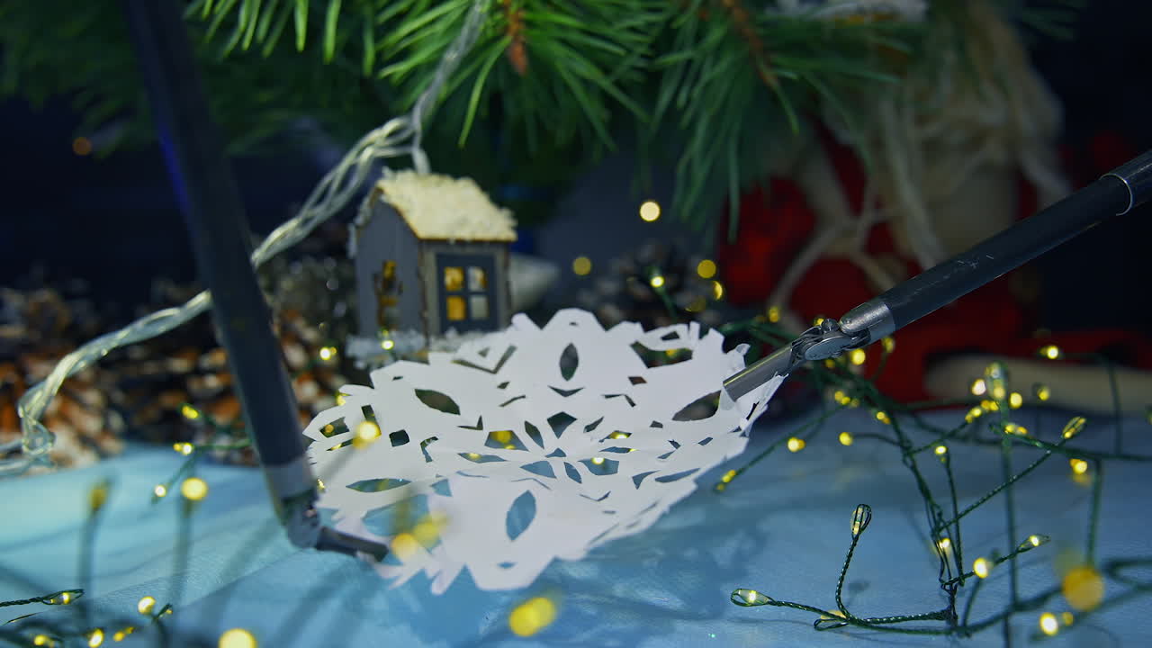 Robotic manipulators for microsurgery hold and stretch the paper snowflake. Christmas tree and ornaments at the backdrop in blur. Close up.