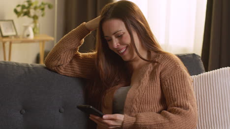 woman sitting on sofa at home using mobile phone to check social media message and scrolling online 15