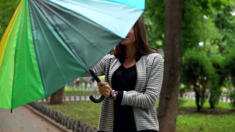 retrato de una joven atractiva mujer morena con su colorido paraguas en sus manos comprobando si está lloviendo en el parque de la ciudad