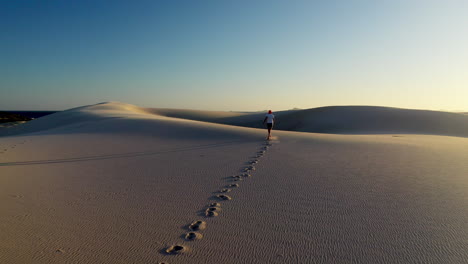 Tiro-De-Dron-De-Un-Hombre-Corriendo-Por-Una-Duna-De-Arena-En-El-Punto-Oscuro-Dunas-De-Arena-En-El-Nido-De-Halcones,-Nueva-Gales-Del-Sur,-Australia