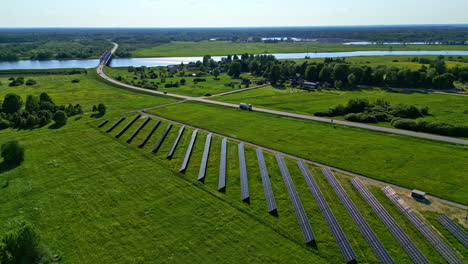 solar panel farm built near countryside road with bridge over vast river, aerial view