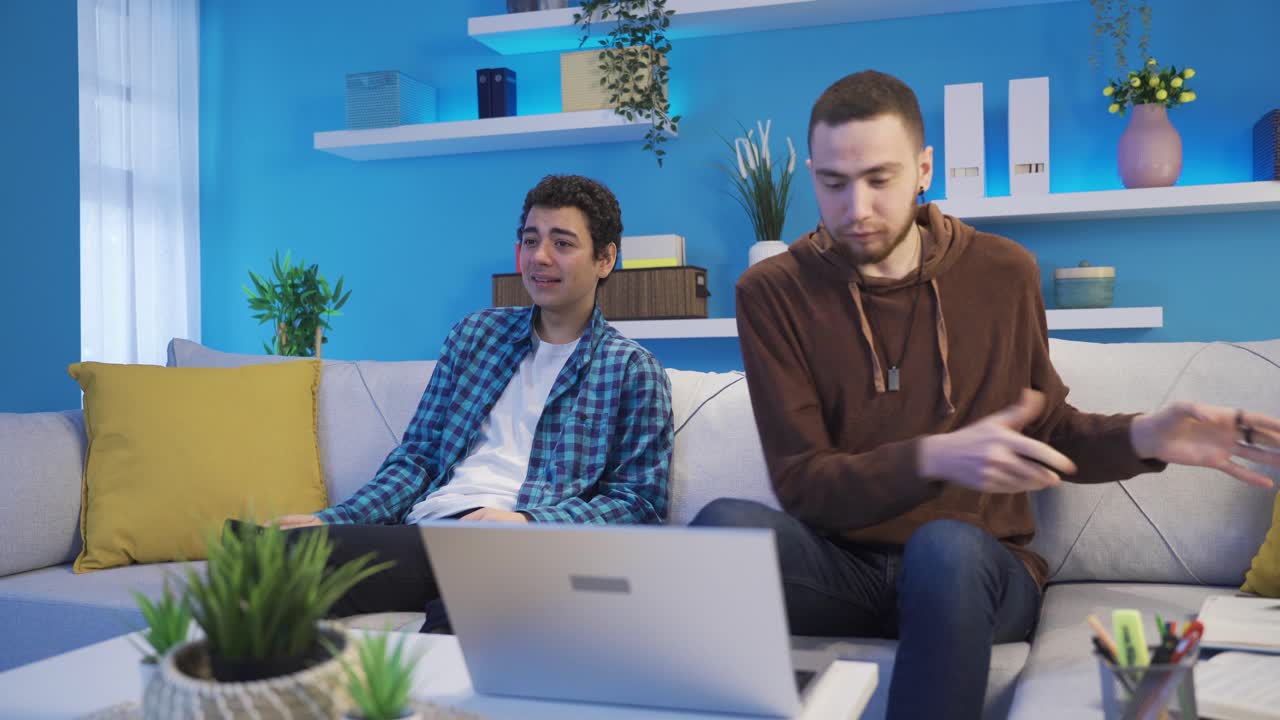 노트북을 사용하여 공부하는 젊은 남자가 그의 남동생에게 화를 내고 불편해집니다.