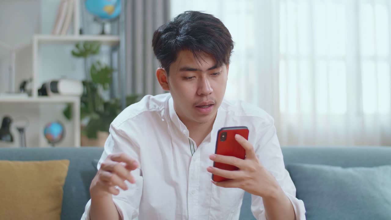 Happy Asian Man Drinking Coffee While Using Smartphone In The Living Room