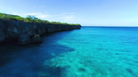 Drone-dolly-along-steep-Caribbean-cliffside-above-clear-blue-ocean-water,-copy-space