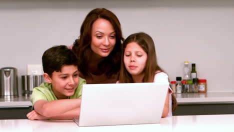 madre usando computadora portátil con sus hijos en la cocina