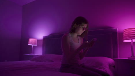 girl picks up phone and looks through social media on smart phone late at night in bedroom.