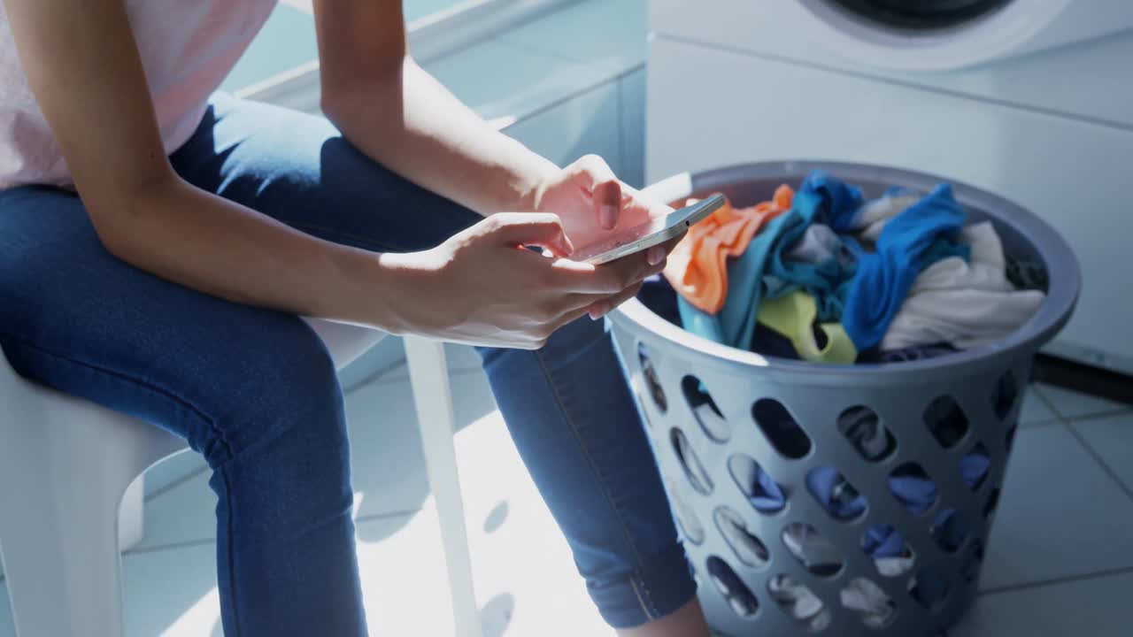 Woman using mobile phone at laundromat 4k