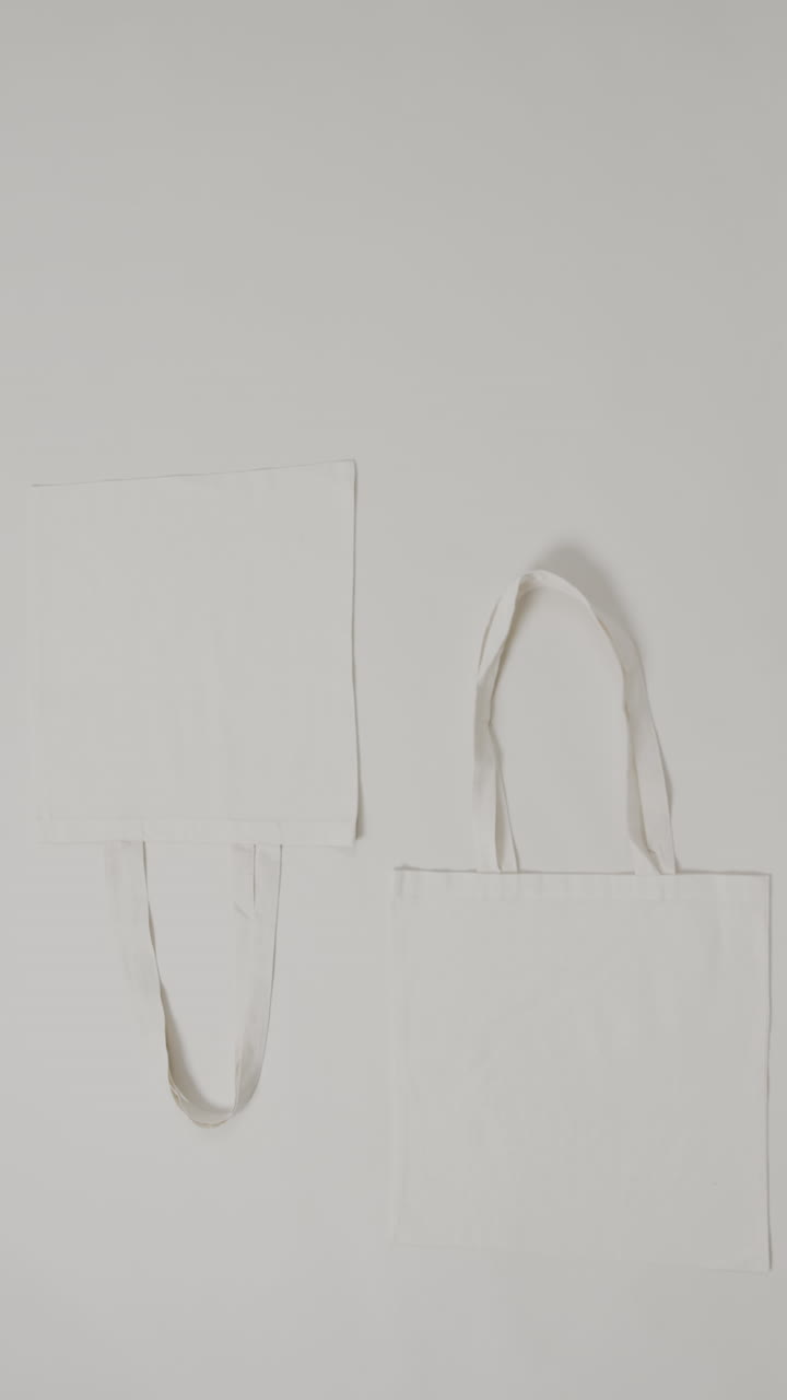 Vertical video of white bags on grey background, copy space, slow motion