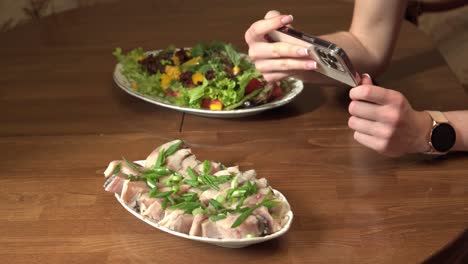 Female hands take pictures of plates of food on the table using a modern smartphone.