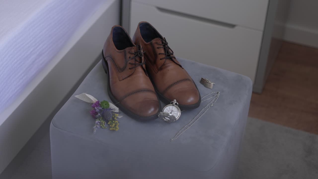 groom's shoes with pocket watch boutonniere and jewelry laid on soft velvet stool